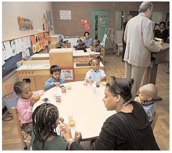 Former U.S. Secretary of Agriculture Dan Glickman promotes federal food programs at a daycare center while the children behind him enjoy lunch. [Photograph by Mike Derer. AP/Wide World Photos. Reproduced by permission.]
